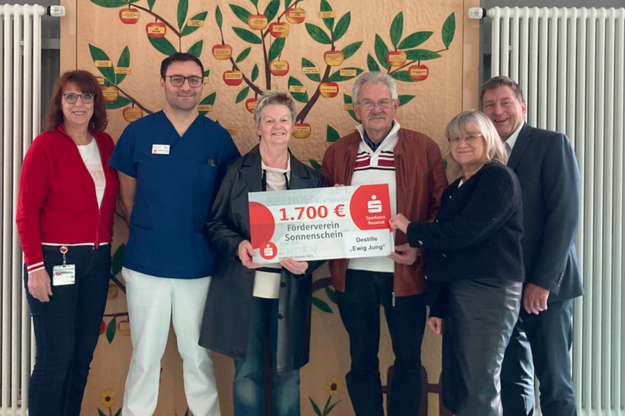 Sechs Personen stehen vor einem Baum-Motiv mit Äpfeln. Eine Person hält ein Schild mit '1.700 €' und 'Sonderverein Sonnenschein'.
