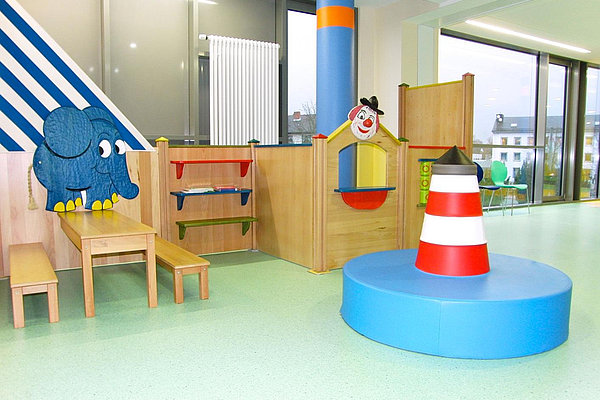 Kinderspielecke mit Holzmöbeln, einem blauen Elefanten an der Wand und einem Spielturm mit rot-weißem Leuchtturmmotiv