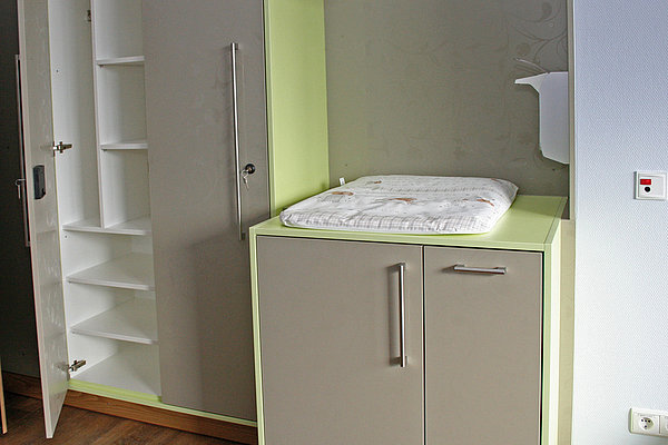 Wickeltisch mit gepolsterter Wickelauflage und offenem Schrank mit Regalfächern in einem hellen Raum
