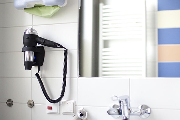 Waschbecken mit Wasserhahn, Wandspiegel, Haartrockner und Wandspender für Papierhandtücher in einem Badezimmer