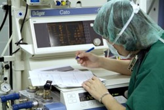Medizinisches Personal in Schutzkleidung dokumentiert Daten an einem Überwachungsgerät im Krankenhaus