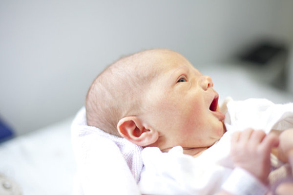 Neugeborenes Baby liegt auf einer weißen Decke und gähnt