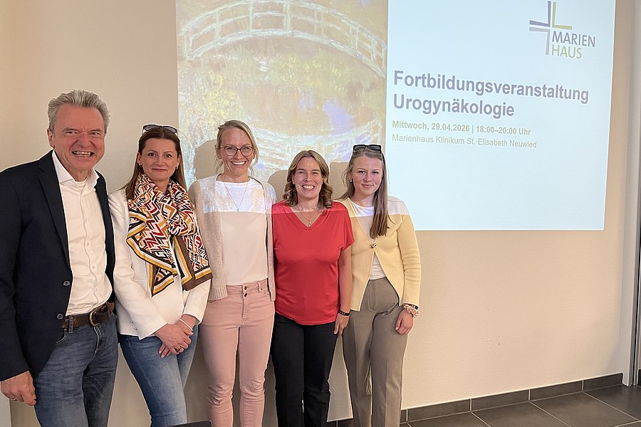 Fünf Personen stehen nebeneinander vor einer Wand mit einem Projektionsbild zur Fortbildungsveranstaltung Urogynäkologie im Marienhaus.