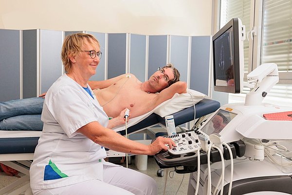 Ärztin führt Ultraschalluntersuchung am Oberkörper eines Mannes durch, der auf einer Untersuchungsliege liegt