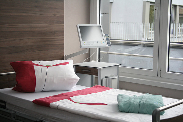 Krankenhauszimmer mit Bett, medizinischem Monitor und Fenster mit Blick nach draußen
