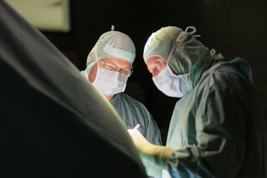Zwei Chirurgen in Operationskleidung und Mundschutz bei einem Eingriff unter OP-Licht