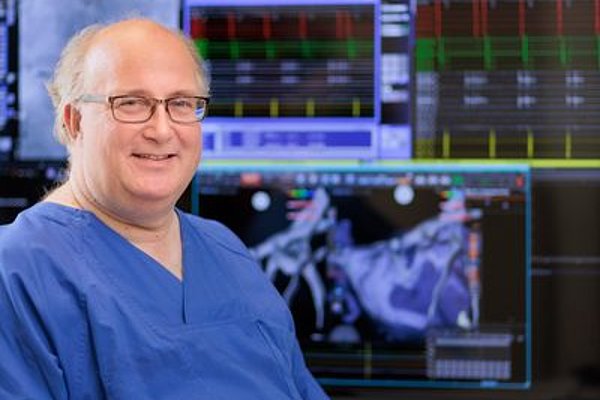 Dr. Hügl, Chefarzt für Innere Medizin-Kardiologie/Rhythmologie, in blauer Arztkleidung vor medizinischen Monitoren mit Herz- und Bilddaten