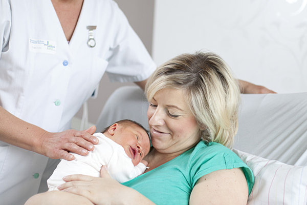 Hebamme legt Neugeborenes behutsam in die Arme der Mutter im Krankenhauszimmer