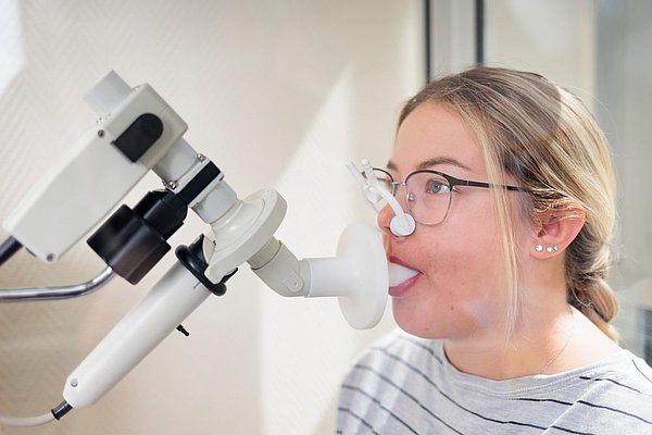 Frau mit Brille führt einen Lungenfunktionstest durch, indem sie in ein Mundstück eines medizinischen Geräts bläst