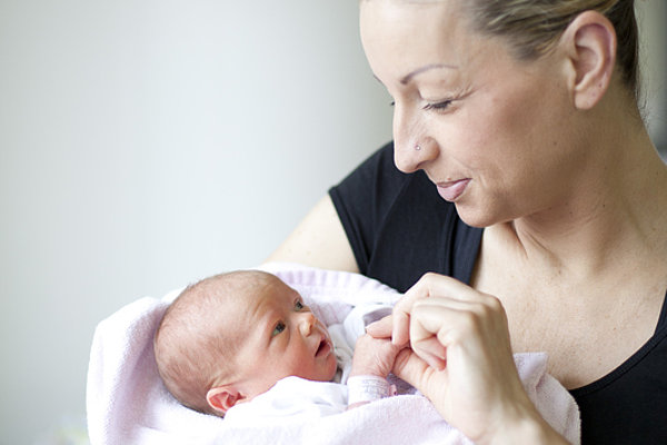 Frau hält Neugeborenes in rosa Decke und schaut liebevoll auf das Baby
