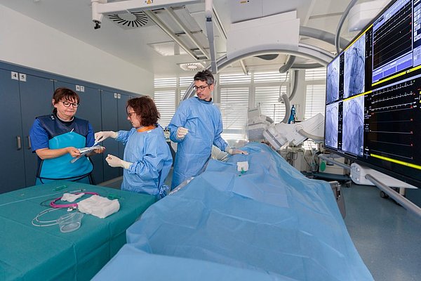 Dr. Geißler und Team führen Herzkatheteruntersuchung in modernem OP-Saal mit Monitoren und medizinischer Ausrüstung durch