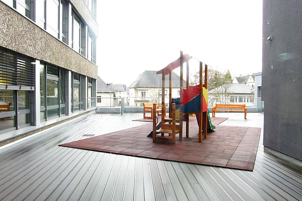 Kleiner bunter Spielplatz mit Rutsche und Klettergerüst auf Dachterrasse eines Gebäudes
