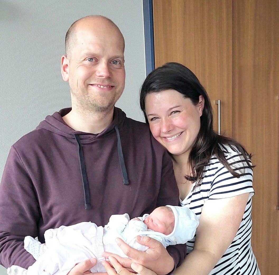Zwei Erwachsene halten gemeinsam ein schlafendes Baby in weißen Kleidern