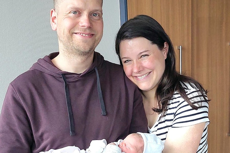 Zwei Erwachsene halten gemeinsam ein schlafendes Baby in weißen Kleidern