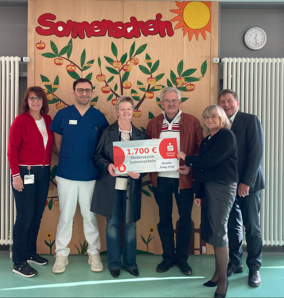 Sechs Personen stehen vor einem Baum-Motiv mit Äpfeln. Eine Person hält ein Schild mit '1.700 €' und 'Sonderverein Sonnenschein'.