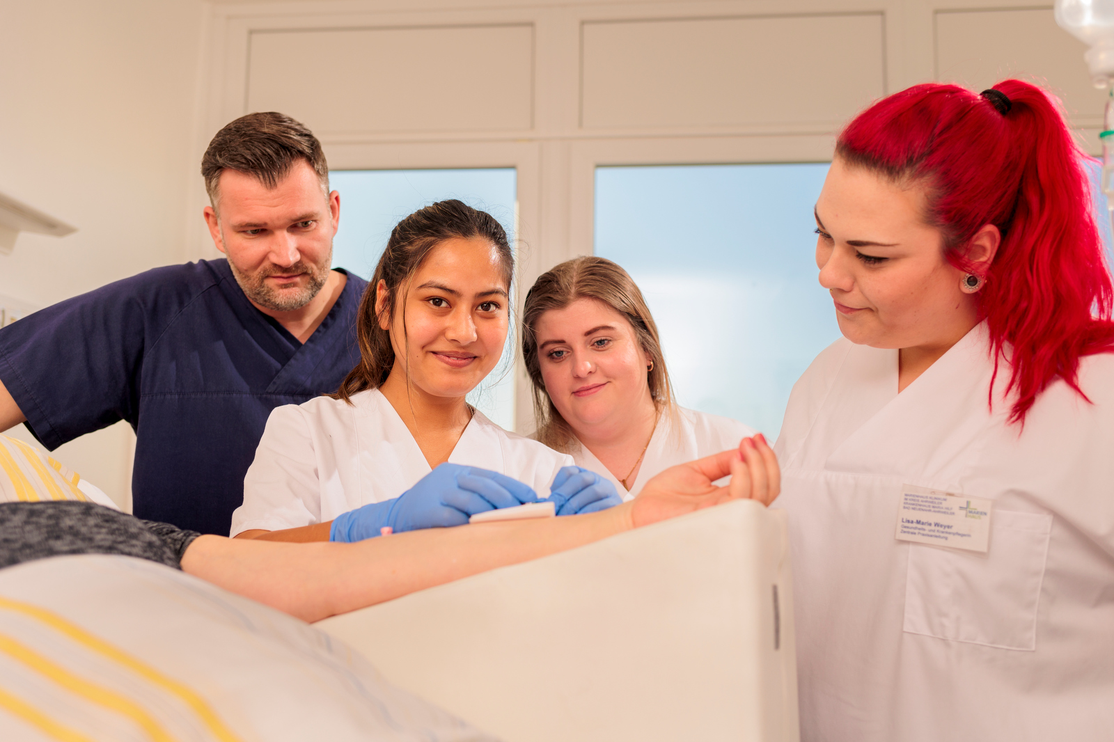 Vier medizinische Fachkräfte in weißer Arbeitskleidung betreuen einen Patienten im Bett